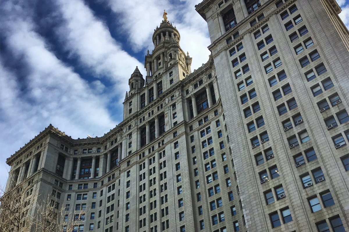 Upward view of a municipal government office tower against a clouded sky.